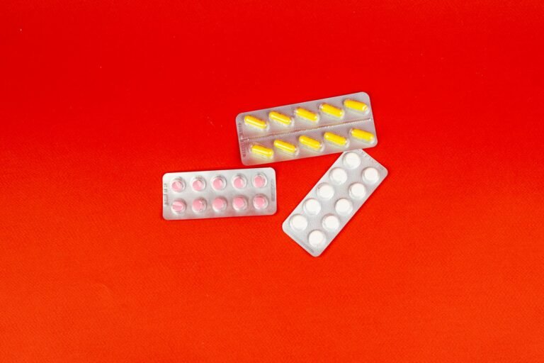 A vivid still life of various medication tablets and capsules on a bright red background.